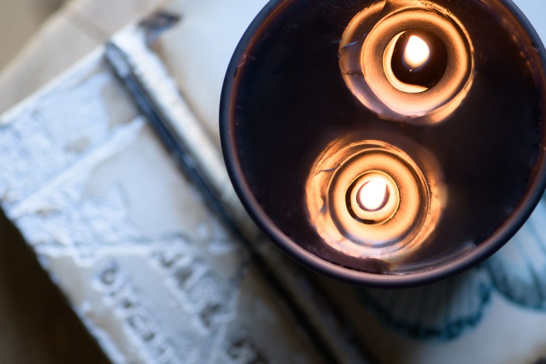 flat lay image looking over the top of a black two wick candle that is lit with the wax pooling