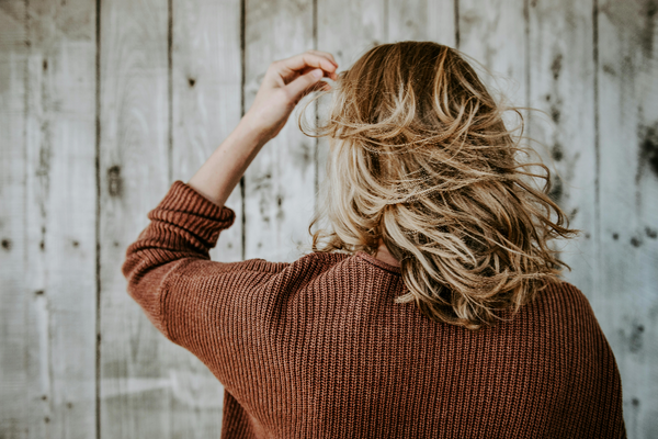 a woman wearing a brown cardi with short blonde hair with her back to the camera