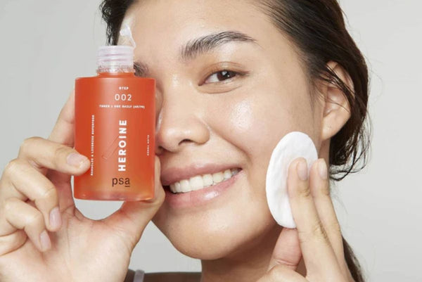 woman smiling holding a bottle of PSA HEROINE Mandelic & Licorice Superfood Glow Toner