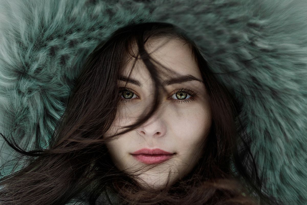 close up of woman's face wearing a fur hat with dark hair across her face