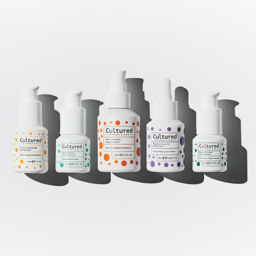 Five white pump bottles of Cultured Cosmetics skincare products arranged vertically in a staggered row against a light gray background with dark gray shadows.