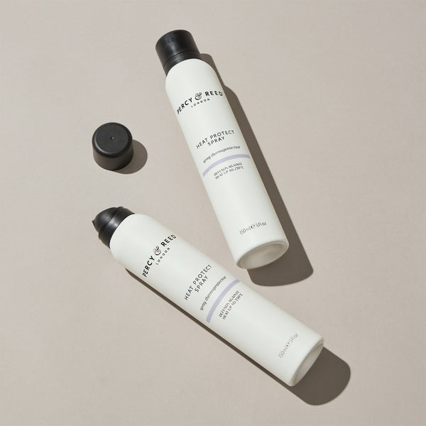 Two white bottles of FRACT OF REEFS hair protectant spray with black caps, one bottle shown with its cap off on a neutral beige background.