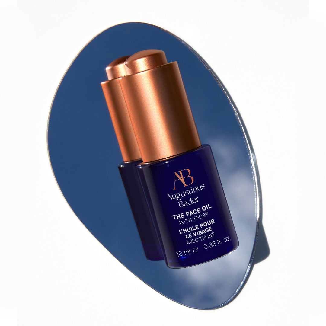 Blue bottle with bronze cap of Augustinus Bader face oil on a blue background
