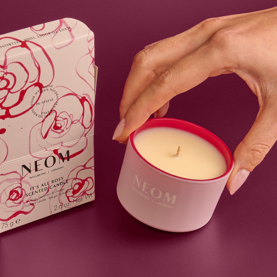 Neom scented candle with a hand holding it and the packaging on a purple background