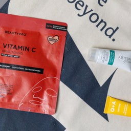 Beauty product packaging including a red vitamin C face mask and two tubes on a patterned surface.