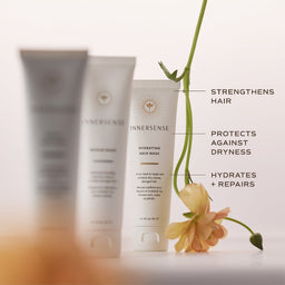 Three Innersense hair care tubes on a white surface with decorative text callouts and a peach flower. The center tube is in focus and reads 'Hydrating Hair Mask,' while the two tubes behind it are blurred.