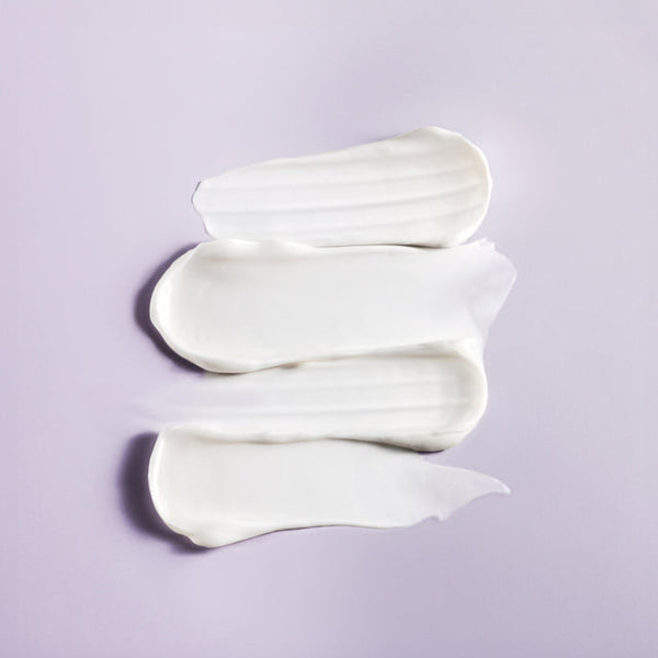 Three swatches of thick white cream or lotion arranged vertically on a light lavender background.