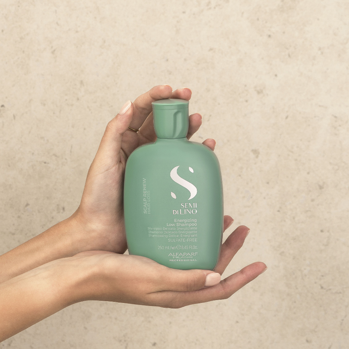 Hand holding a green bottle with a brand logo against a beige background