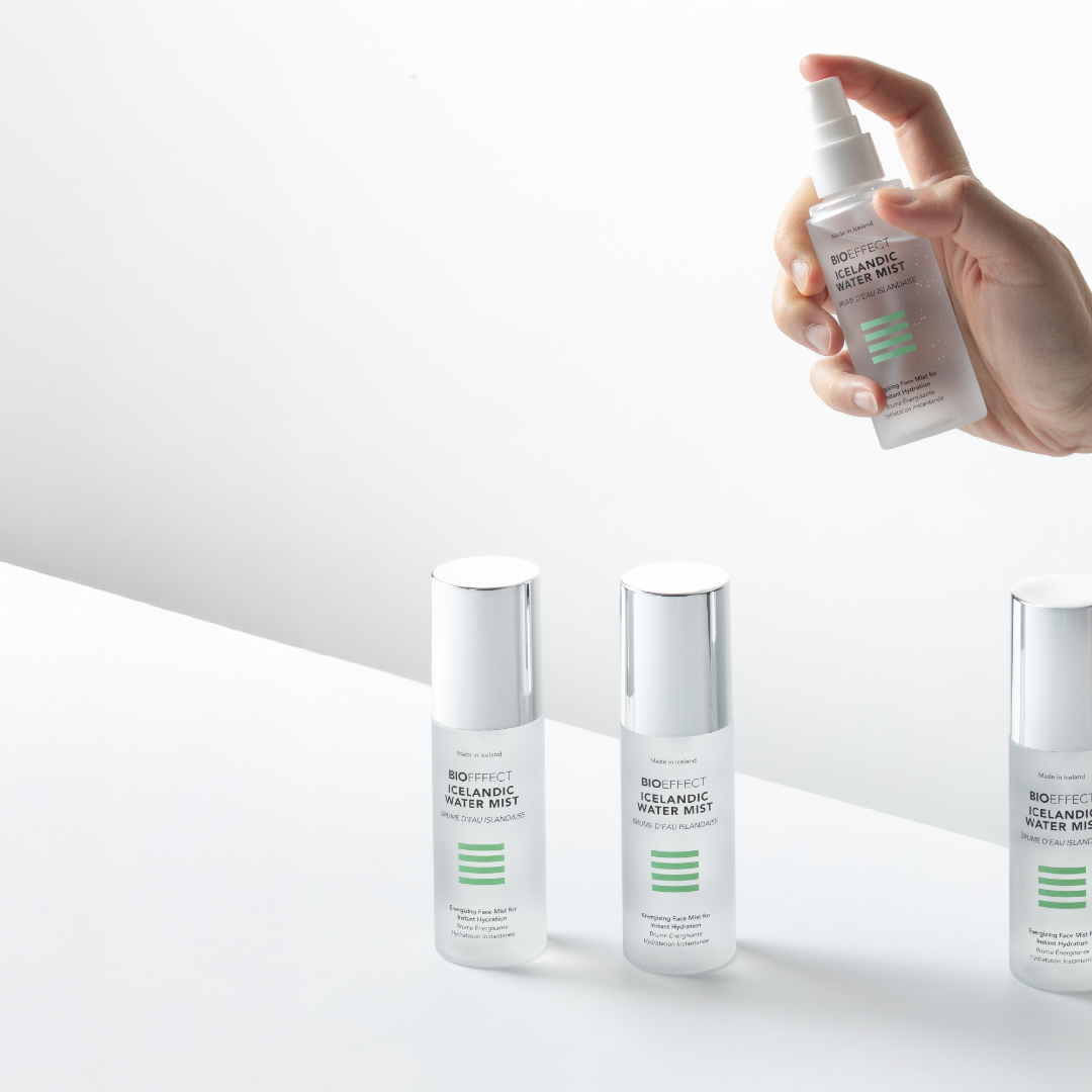 Hand holding a skincare product with other skincare bottles on a white background