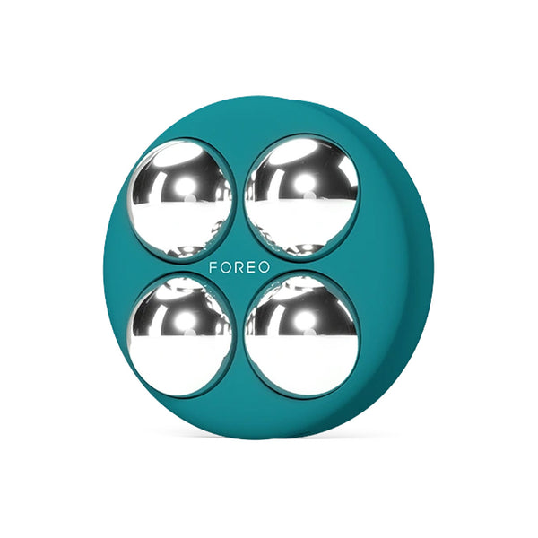 A round teal silicone personal massager with four metallic silver spheres, featuring the brand name 'FOREO' printed in white in the center, on a solid white background.