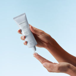 Hand holding a tube of KeraSilk hair care product against a light blue background