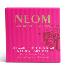 Bright pink square product box for a NEOM Wellbeing London Ceramic Shooting Star Natural Diffuser, featuring gold and white text and a small cafe-and-tree illustration on a white background.