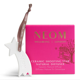 A white ceramic shooting star diffuser ornament with a brown ribbon, shown next to its bright pink NEOM brand packaging box on a clean white background.
