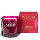 A NEOM Wellbeing London 'Christmas Wish' scented candle in a deep magenta glass jar, shown next to its red packaging box with gold lettering on a white background.