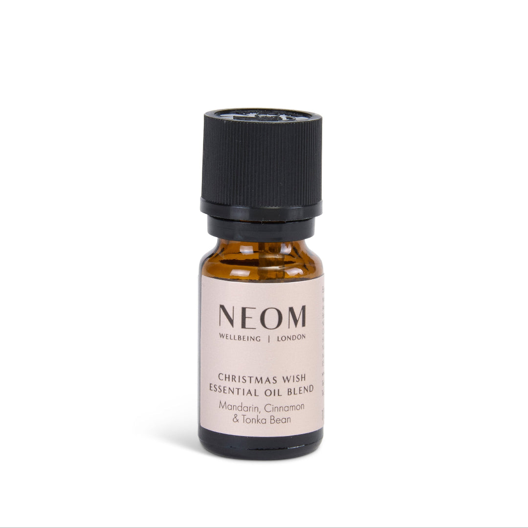 A small amber glass bottle of NEOM Welcoming London Christmas Wish Essential Oil Blend with a black cap and a cream label, set against a plain white background.