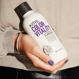 KMS Color Vitality shampoo bottle held in a hand against a neutral background