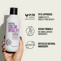 KMS Color Vitality shampoo bottle held by a hand with PETA approval and vegan formula labels on a beige background.