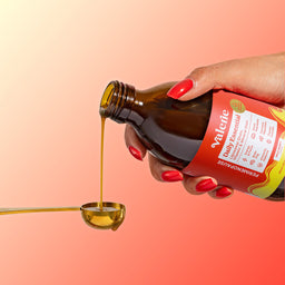 Hand pouring oil from a bottle labeled 'Valerie' onto a spoon against a gradient background