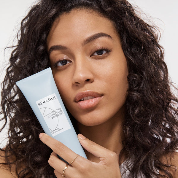Woman holding a blue hair care product with a neutral background