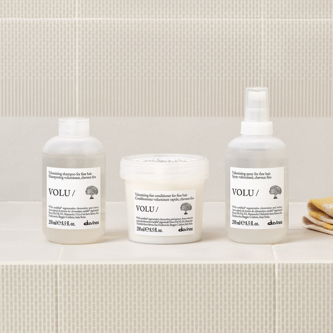 Three Davines hair care products on a bathroom shelf with a tiled wall background.