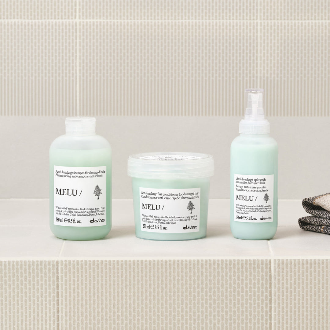 Three Melu hair care products on a bathroom counter with a tiled wall background.