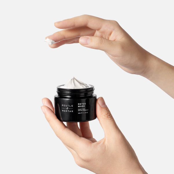 Hand holding a jar of 'Festle & Mortar Detox Mask' against a white background