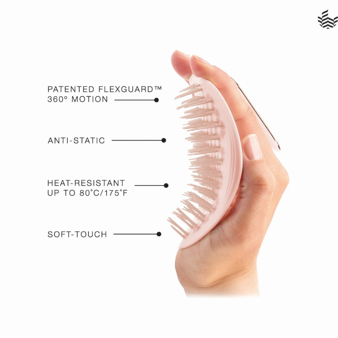 A hand holds a light pink oval hairbrush with soft bristles against a white background, with text callouts reading 'PATENTED FLEXGUARD 360° MOTION,' 'ANTI-STATIC,' 'HEAT-RESISTANT UP TO 80°C/175°F,' and 'SOFT-TOUCH.'.