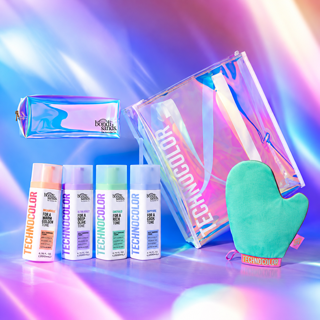A beauty gift set from both sides featuring Technocolor hair products, including four spray bottles, a holographic makeup pouch, a large holographic tote bag, and a mint green silicone oven mitt, arranged on a vibrant, multicolored light streak background.