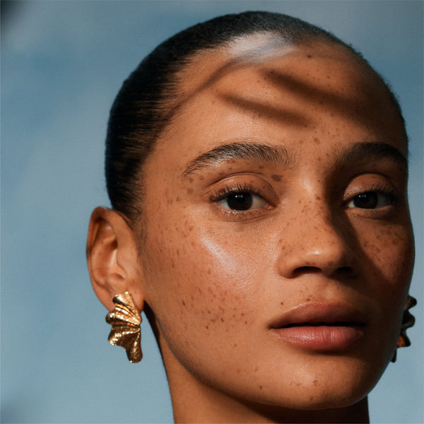Close-up of a person wearing gold earrings against a blue background