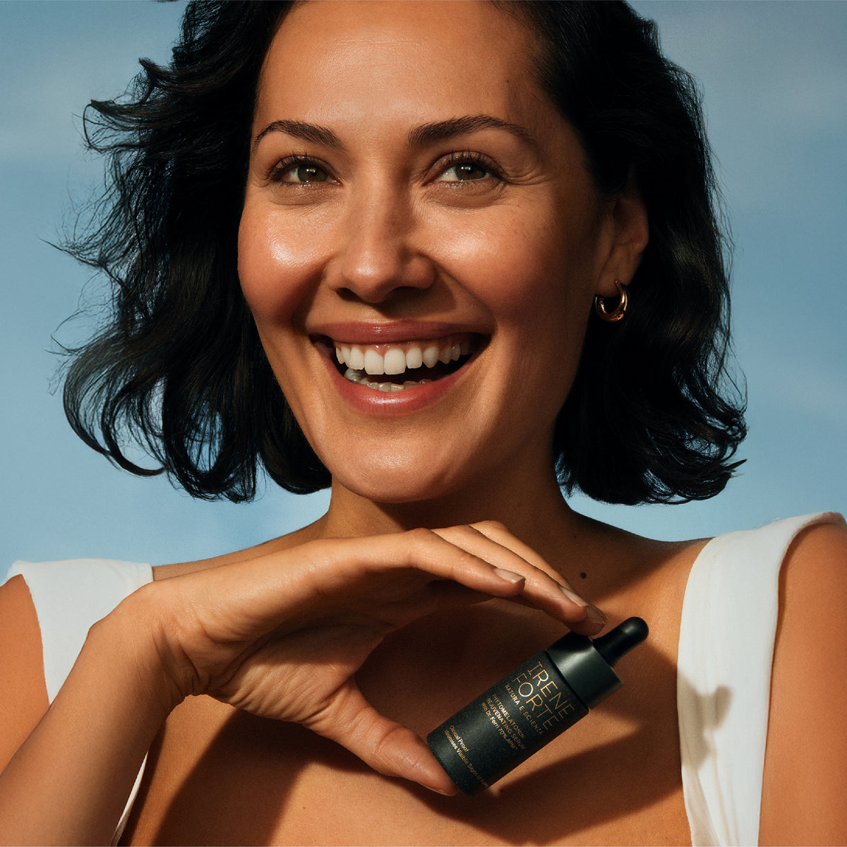 Woman holding a skincare bottle against a blue sky background