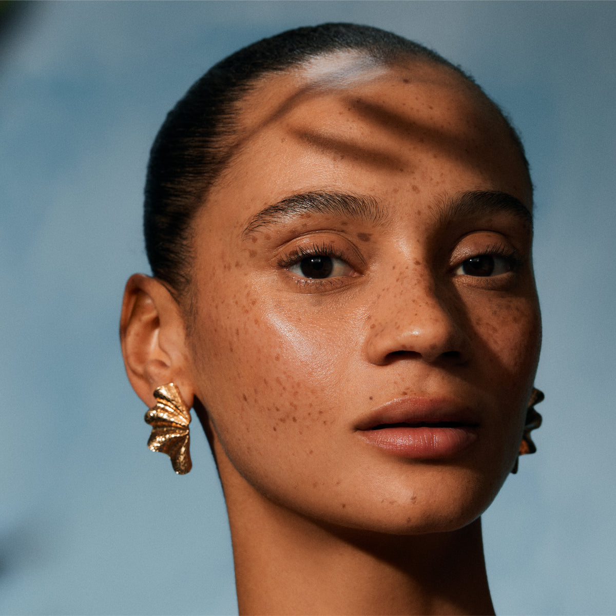 Close-up of a person wearing gold earrings with a blurred background