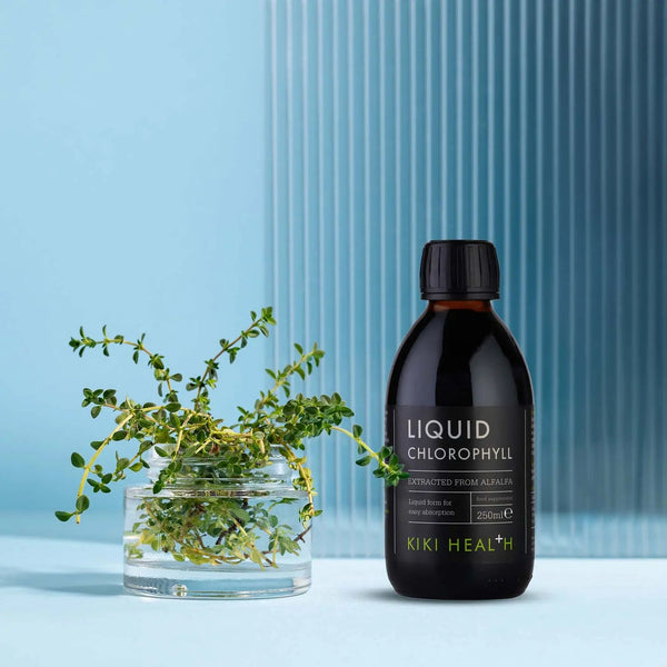 Bottle of KIKI Health Liquid Chlorophyll with a glass of water and green leaves on a blue background
