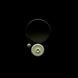 Three circular glass objects, including two larger dark-toned pieces and one pale greenish-beige piece with a small clear droplet, arranged on a solid black background.