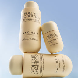 Nak Hair Volume Shampoo and Conditioner bottles stacked on a light blue background