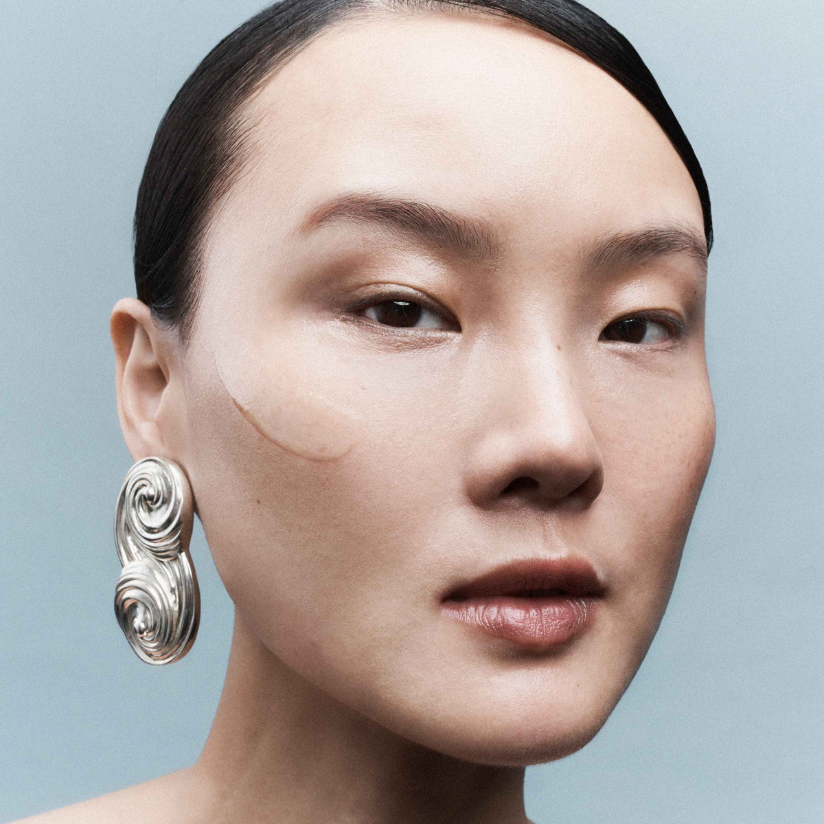 Close-up of a person wearing large, ornate earrings against a light blue background