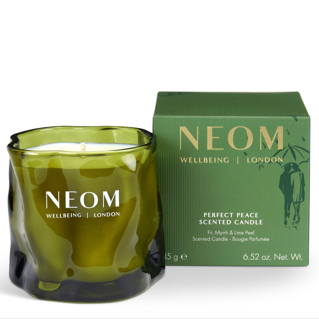 An olive green glass scented candle with a wick and white wax, shown next to its matching green packaging box. The brand NEOM is clearly visible on both the candle and the box.