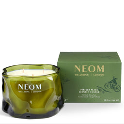 A NEOM Wellbeing London scented candle in a wavy translucent olive-green glass jar, shown next to its matching green packaging box on a white background.