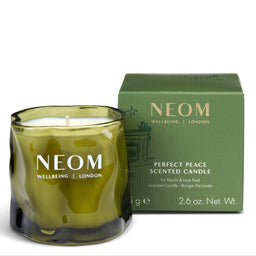 A NEOM Wellbeing London scented candle in a wavy olive-green glass jar, shown next to its matching green box packaging on a clean white background.