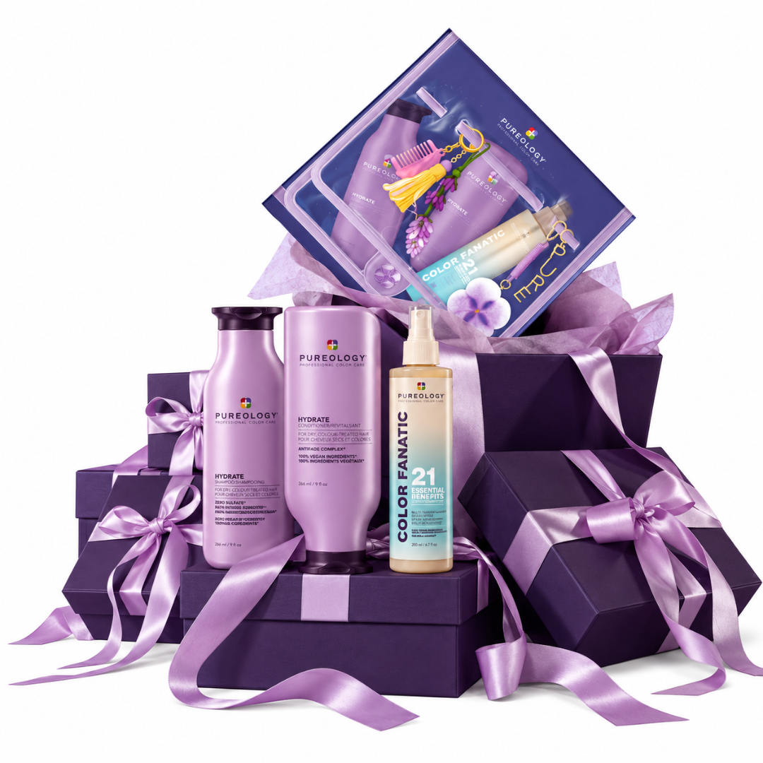 Pureology Color Fanatic hair care gift set arranged in a purple gift box with purple satin ribbons, including a purple shampoo bottle, a purple conditioner bottle, a beige 21-volume treatment bottle, and a purple boxed set leaning behind.