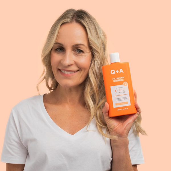Woman holding an orange bottle of Q+A shampoo against a peach background