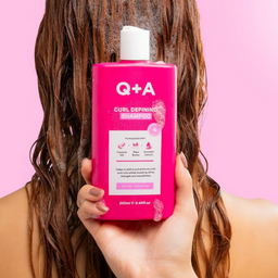 Person holding a pink bottle of Q+A Curl Defining Shampoo against a pink background
