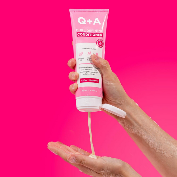 Hand holding a tube of Q+A hair conditioner with pink background