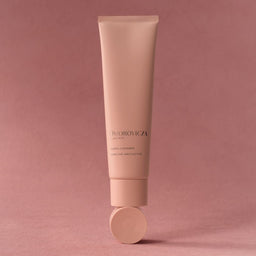 A single tube of Dhorovica Clear Skin Cleanser in a soft dusty pink color, standing upright on its cap against a matching solid pink background.