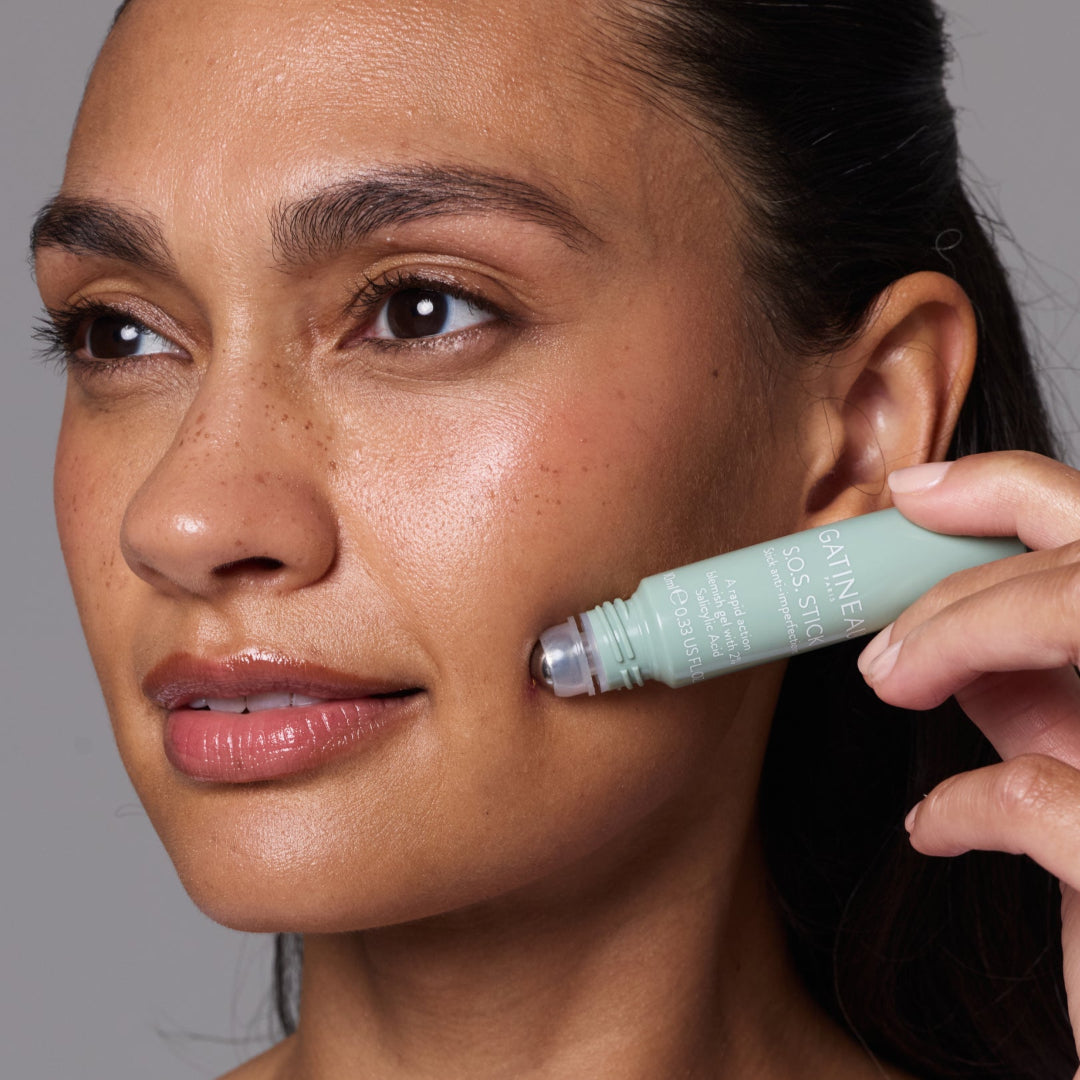 Woman applying a cosmetic product to her face with a focus on the product's branding.