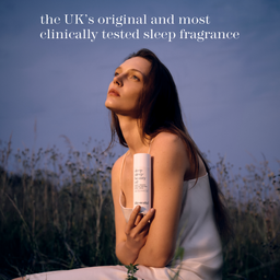 A woman in a white dress sits outdoors in a field at dusk, holding a white bottle labeled dr. merck sleep clarity.
