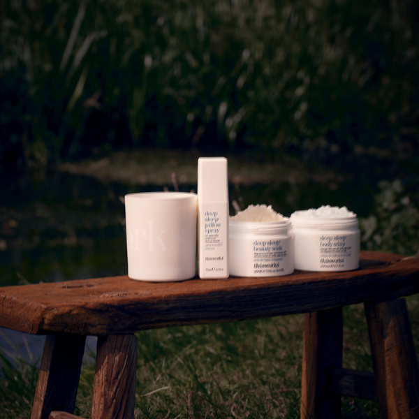 Four white skincare products from the brand Deep Dive Beauty stand on a rustic wooden bench outdoors, with a blurred green garden background.