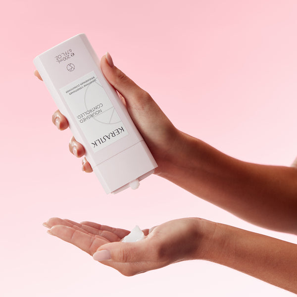 Hand holding a skincare product with a pink background