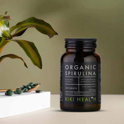 Bottle of Organic Spirulina tablets by KIKI Health on a neutral background with a plant.
