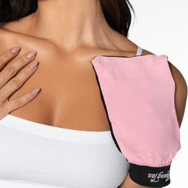 a woman applying self tanning lotion with a pink glove