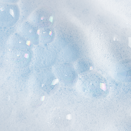 A close-up of pale blue and white foamy texture with translucent bubbles and scattered iridescent square pieces.